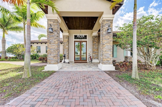 view of exterior entry with stone siding, french doors, and stucco siding