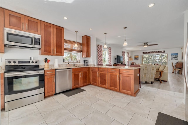 kitchen featuring open floor plan, light stone counters, brown cabinets, a peninsula, and stainless steel appliances