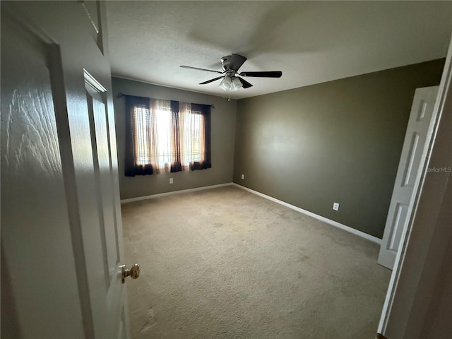 carpeted empty room featuring a ceiling fan and baseboards