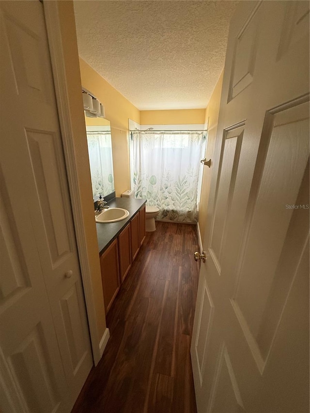 full bath with toilet, a textured ceiling, wood finished floors, and vanity