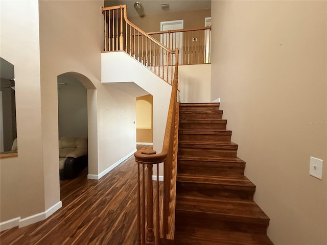 stairway with arched walkways, wood finished floors, a towering ceiling, and baseboards