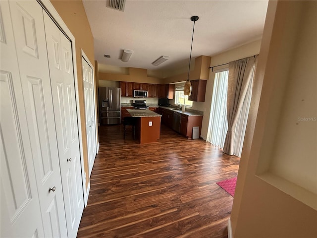 kitchen featuring a center island, visible vents, hanging light fixtures, appliances with stainless steel finishes, and dark wood-type flooring