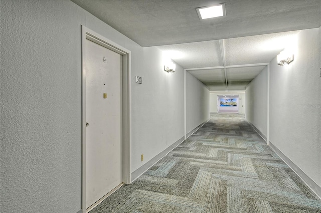 hall with carpet flooring, a textured wall, and baseboards