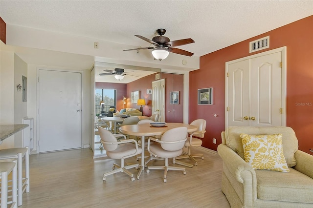dining area with light wood-style flooring, ceiling fan, a textured ceiling, and baseboards