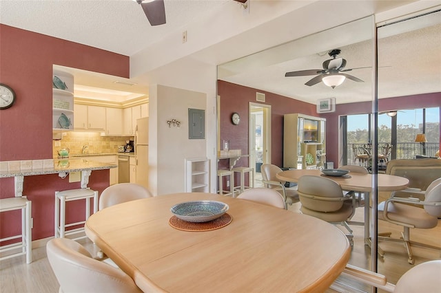 dining space with ceiling fan, a textured ceiling, light wood-style flooring, and electric panel