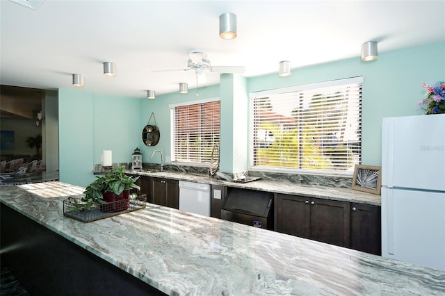 kitchen featuring white appliances, dark brown cabinets, light stone counters, and a sink