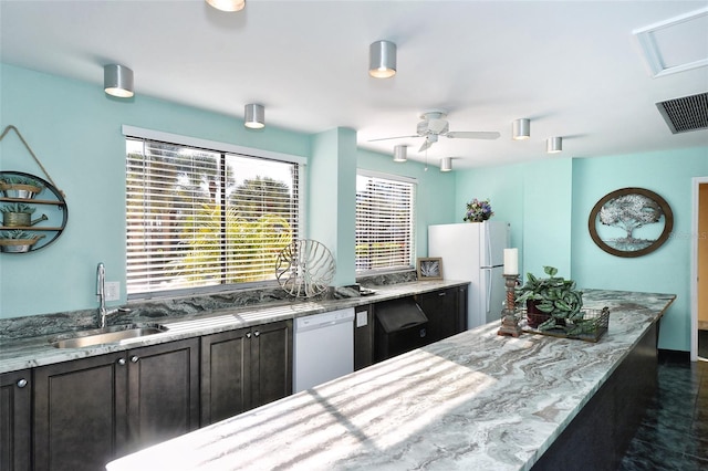 kitchen with a sink, white appliances, ceiling fan, and light stone counters