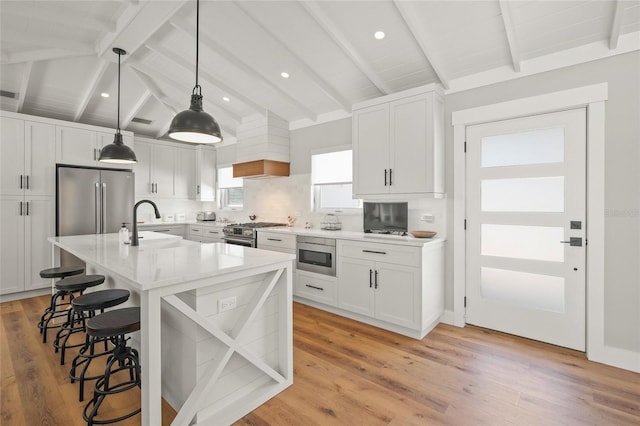 kitchen featuring a breakfast bar area, vaulted ceiling with beams, a sink, stainless steel appliances, and light countertops