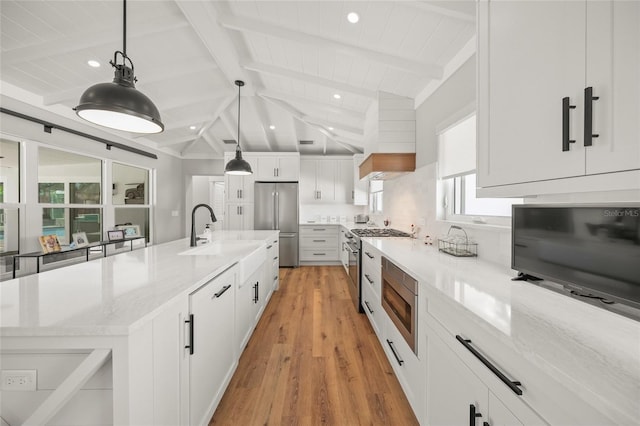 kitchen with a sink, light stone counters, white cabinetry, appliances with stainless steel finishes, and vaulted ceiling with beams