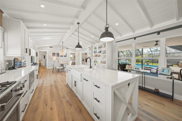 kitchen featuring white cabinets, vaulted ceiling with beams, high end stainless steel range, and a sink