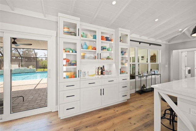 interior space with a ceiling fan, white cabinetry, light wood-style floors, glass insert cabinets, and lofted ceiling