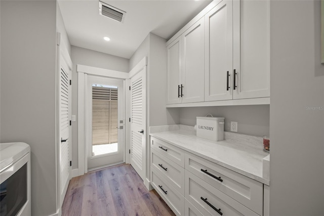 clothes washing area with washing machine and clothes dryer, visible vents, light wood-style flooring, recessed lighting, and cabinet space