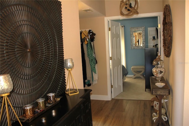 hall featuring visible vents, baseboards, and wood finished floors