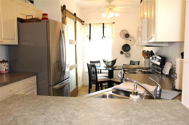 kitchen with a barn door, appliances with stainless steel finishes, ceiling fan, and a sink