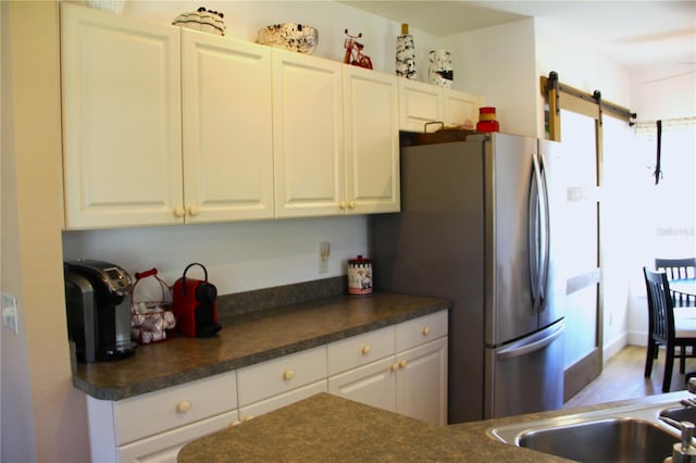 kitchen with freestanding refrigerator, a barn door, dark countertops, and white cabinetry