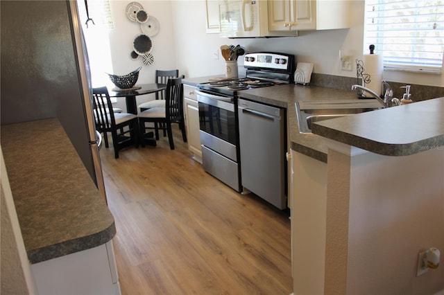 kitchen with stainless steel appliances, dark countertops, a sink, and light wood-style flooring