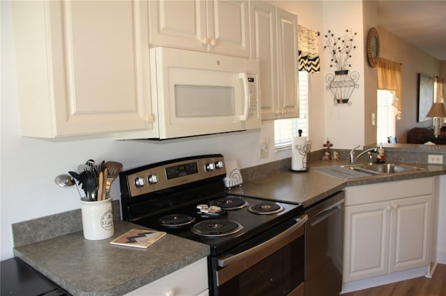 kitchen with appliances with stainless steel finishes, dark countertops, a sink, and white cabinets