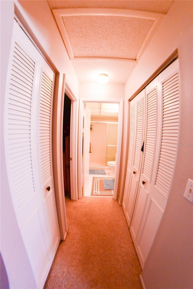 corridor with light colored carpet and a textured ceiling