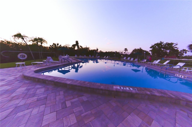 pool at dusk featuring a patio area and a community pool