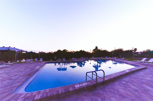 pool at dusk featuring a patio area and a community pool