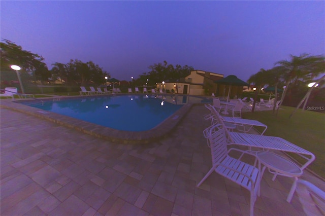 pool at dusk with a patio and a community pool