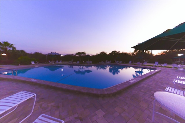 pool at dusk with a patio and a community pool