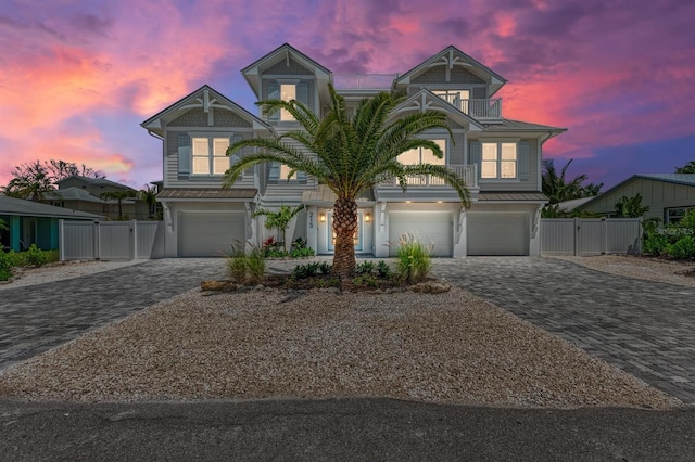 coastal home featuring decorative driveway, a balcony, a gate, and an attached garage