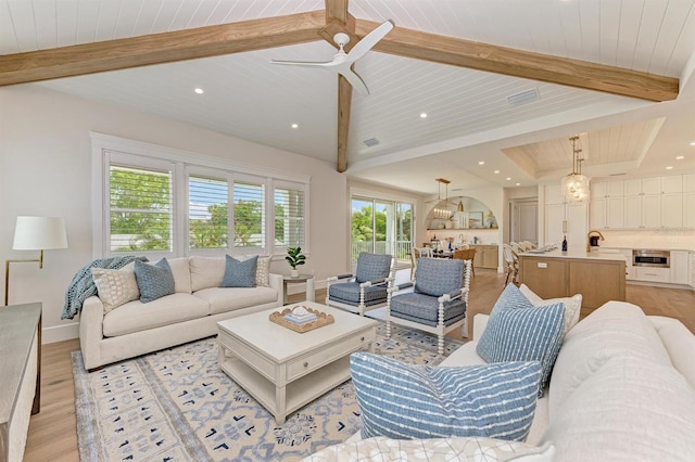 living area with visible vents, baseboards, ceiling fan, lofted ceiling with beams, and light wood-style flooring