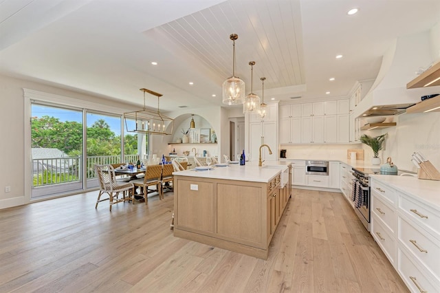 kitchen with custom range hood, light wood-style flooring, high end range, a raised ceiling, and a sink