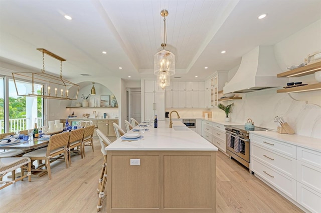 kitchen with custom exhaust hood, a notable chandelier, a raised ceiling, and high end stove