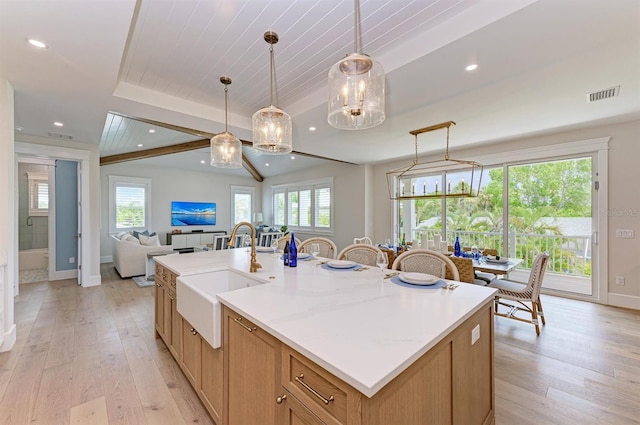 kitchen with visible vents, light wood finished floors, a kitchen island with sink, a sink, and open floor plan