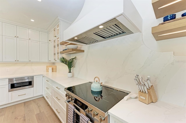 kitchen featuring glass insert cabinets, premium range hood, stainless steel electric range oven, light wood-style flooring, and white cabinets