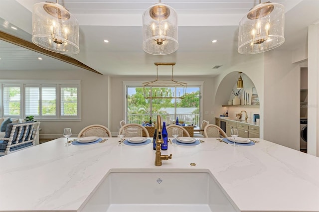 kitchen with light stone countertops, decorative light fixtures, a center island with sink, recessed lighting, and washer / dryer