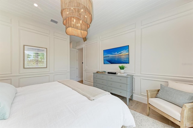 bedroom with wood finished floors, visible vents, an inviting chandelier, wooden ceiling, and a decorative wall