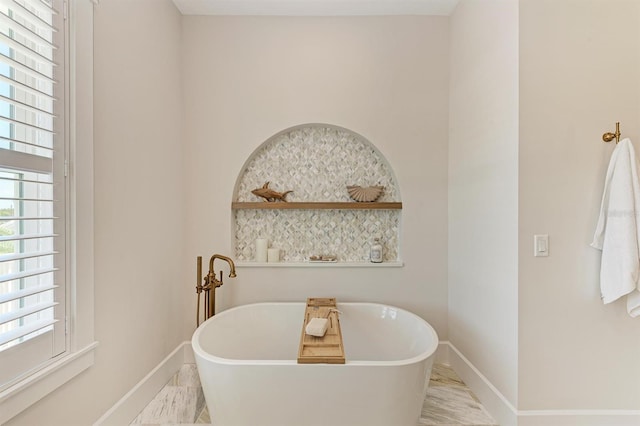 bathroom with baseboards, a freestanding bath, and marble finish floor