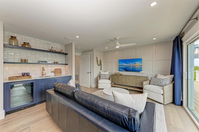 living room featuring visible vents, wine cooler, indoor wet bar, light wood-style flooring, and a decorative wall