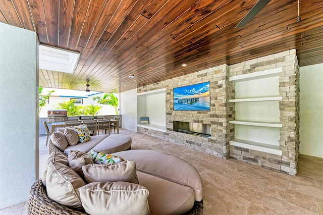 living area featuring a skylight, wood ceiling, and an outdoor stone fireplace