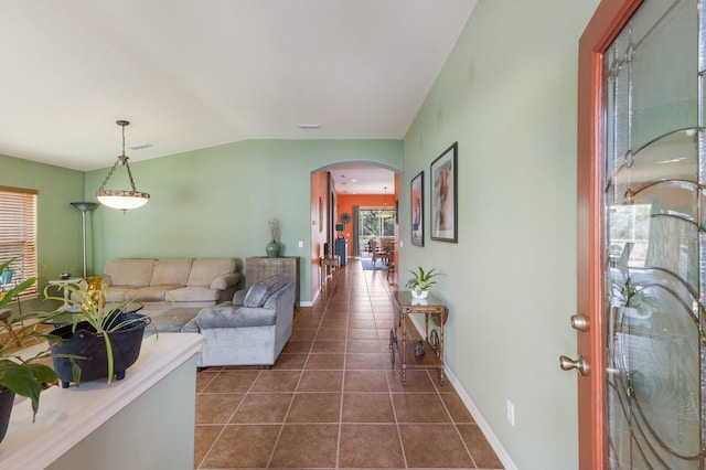 living area featuring arched walkways, dark tile patterned flooring, lofted ceiling, and baseboards