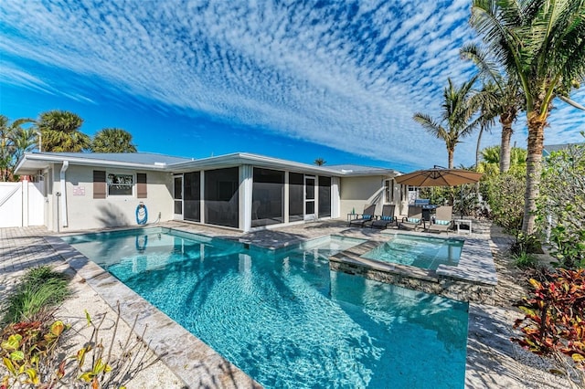 view of pool with a pool with connected hot tub, a sunroom, a patio area, fence, and a gate