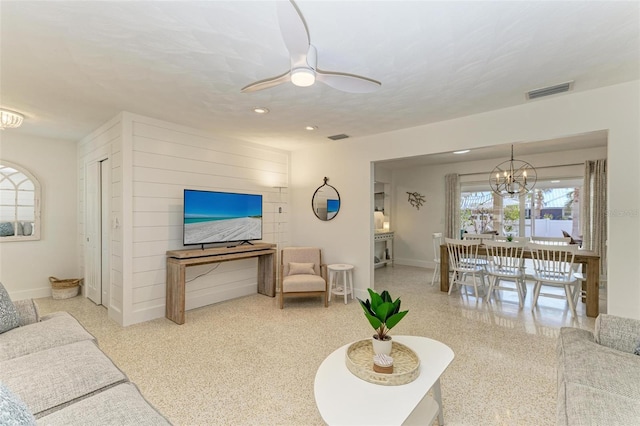 living area featuring ceiling fan with notable chandelier, visible vents, baseboards, and speckled floor