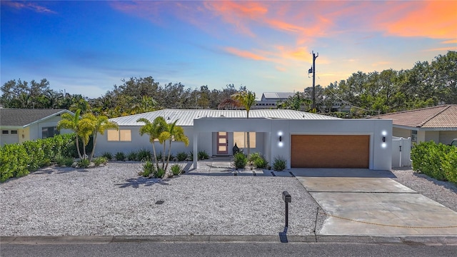 view of front facade with a garage, concrete driveway, metal roof, and stucco siding