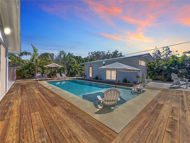 pool at dusk with an outdoor pool and a deck