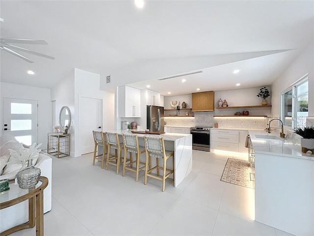 kitchen with a peninsula, a sink, a kitchen breakfast bar, appliances with stainless steel finishes, and open shelves