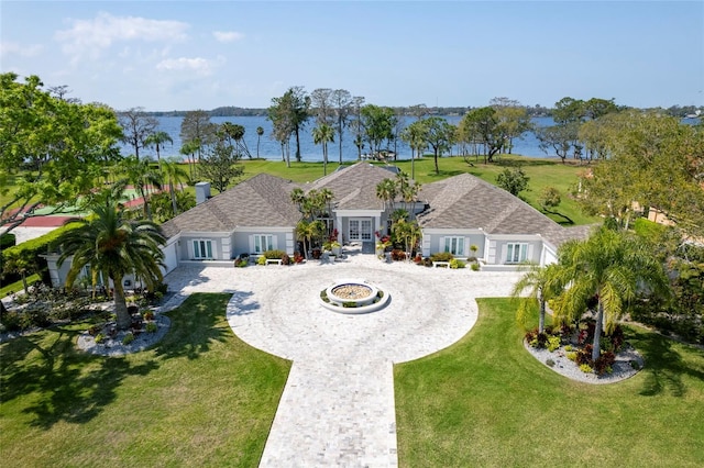 view of front facade with curved driveway, french doors, a front lawn, and a water view