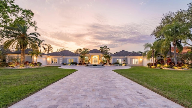 mediterranean / spanish-style home featuring a yard, stucco siding, french doors, a garage, and decorative driveway