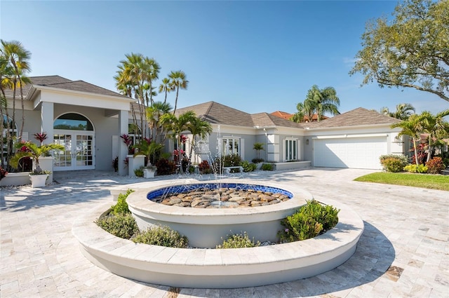 view of front of home with curved driveway, french doors, a garage, and stucco siding