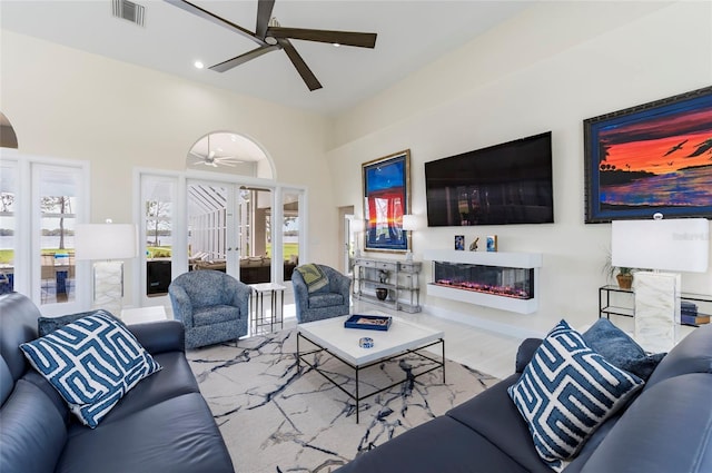 living area with a glass covered fireplace, visible vents, and ceiling fan