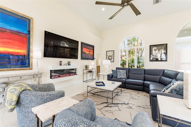 living room featuring visible vents, a glass covered fireplace, and a ceiling fan