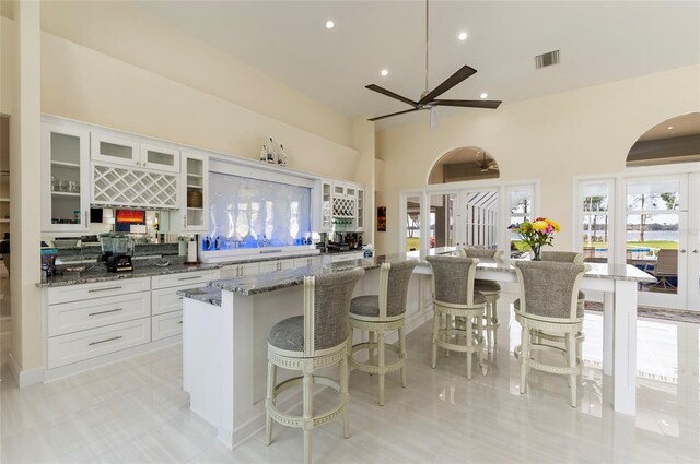 kitchen with visible vents, a spacious island, a high ceiling, white cabinets, and a kitchen breakfast bar