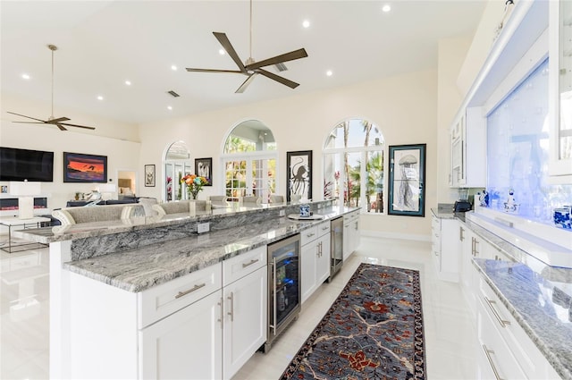 kitchen with light stone countertops, ceiling fan, wine cooler, white cabinets, and open floor plan